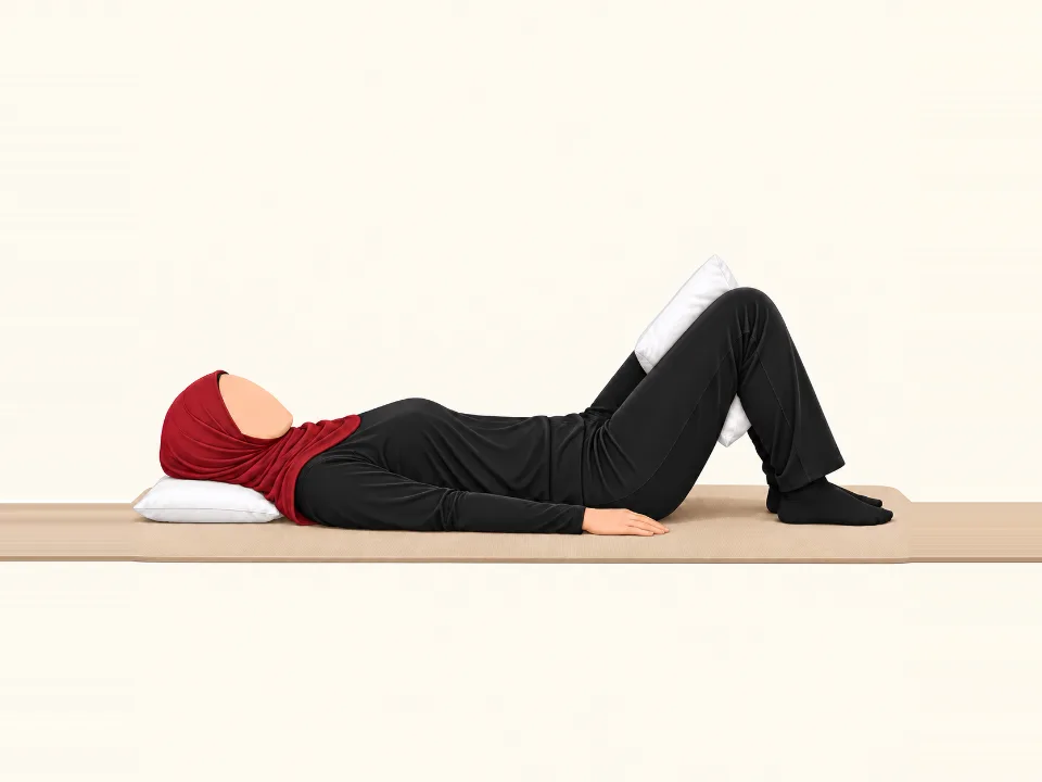 Woman in a red hijab lying on her back with knees bent, squeezing a pillow between her knees.
